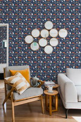 A room with navy blue Halloween-themed wallpaper with small motifs of pumpkins, ghosts, and candy corn. A wooden armchair with a yellow-striped pillow, a side table, and a white sofa are in front of the traditional wallpaper.