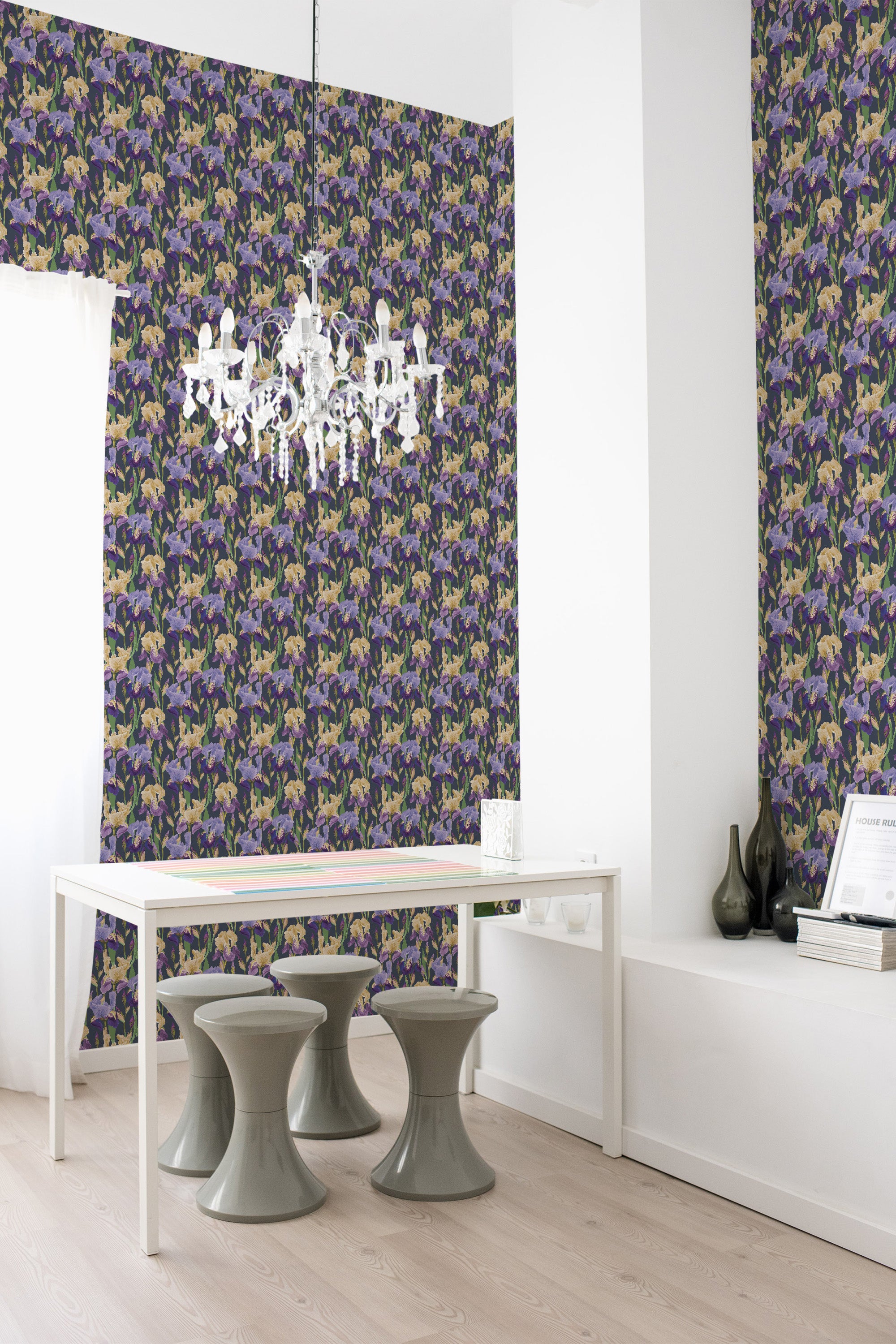 A room with a wall covered in Bold Iris wallpaper with a repetitive pattern of stylized purple and green iris flowers on a dark background, complemented by a modern white desk and elegant lighting, traditional wallpaper.