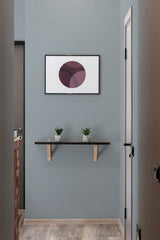 A room with light blue wallpaper with a soft, delicate geometric pattern, complemented by a black-framed abstract artwork, wooden shelf with two potted plants, and a traditional wallpaper.