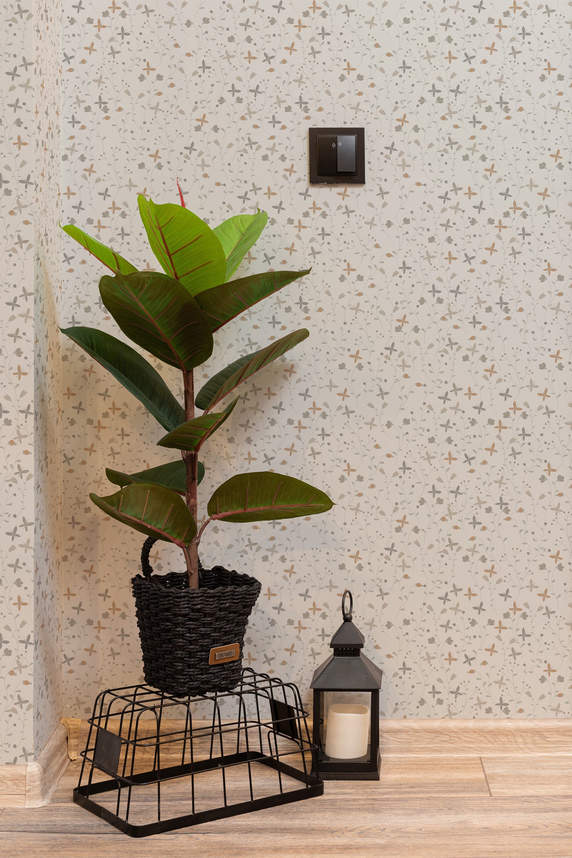 Self-adhesive wallpaper with a subtle Spring cottage design of small flowers and leaves, applied to a room wall, accompanied by a potted plant and a lantern on the floor.