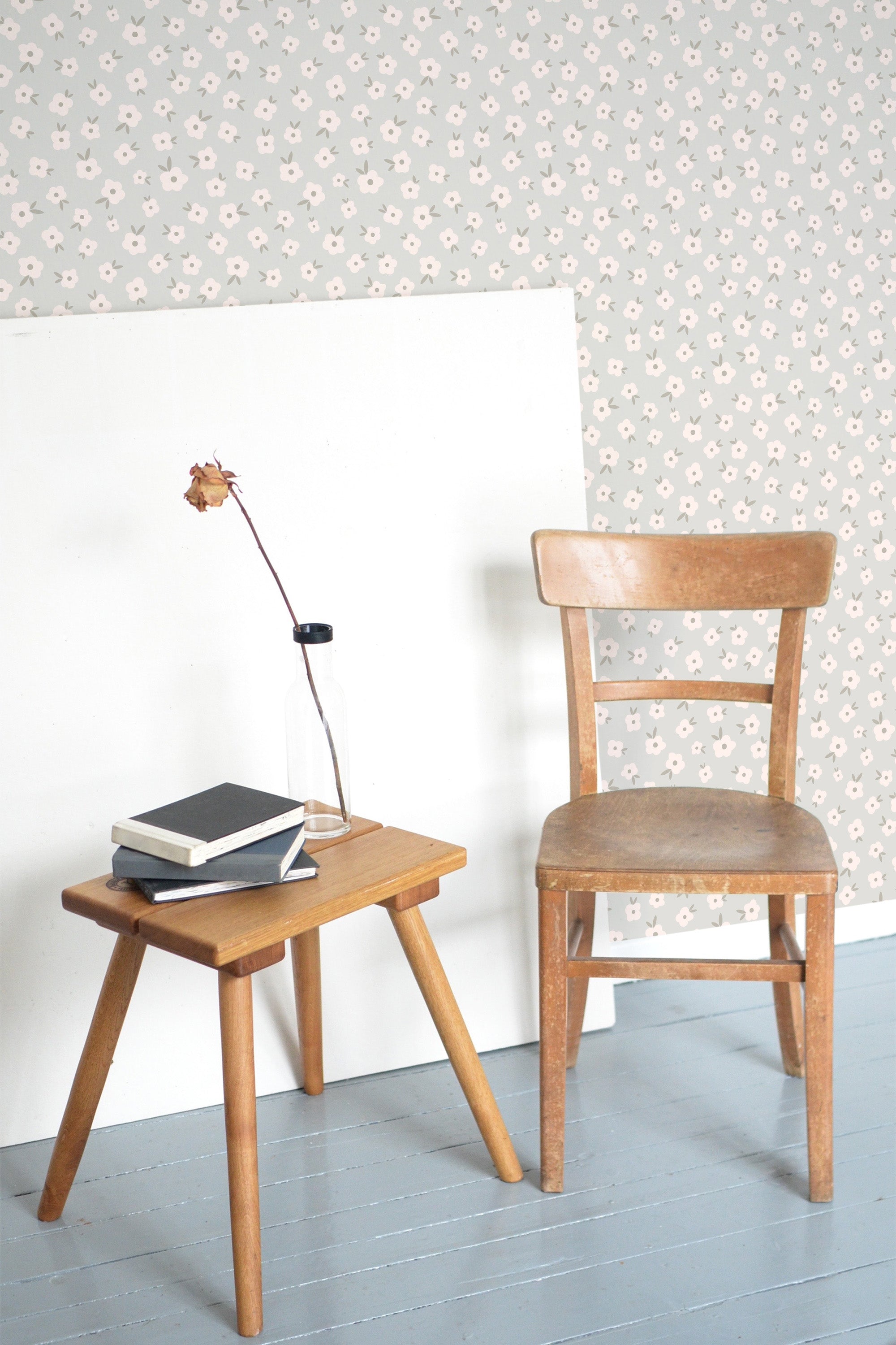 Self-adhesive wallpaper with a neat and cute spring floral design on a room's wall, a chair and side table with books next to it.