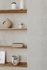 Self-adhesive light gray crocodile pattern wallpaper on a wall with wooden shelves holding various decorative items.