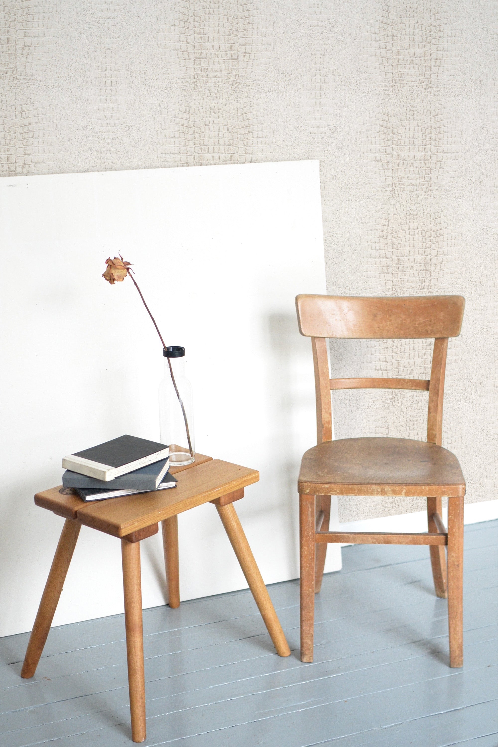 Self-adhesive light beige crocodile pattern wallpaper in a room with a wooden chair, a small table with books, and a floor lamp.