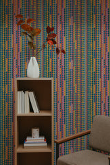 Self-adhesive retro vintage geometric wallpaper with colorful vertical stripes and shapes on a room wall, complemented by a wooden bookshelf and a gray armchair.