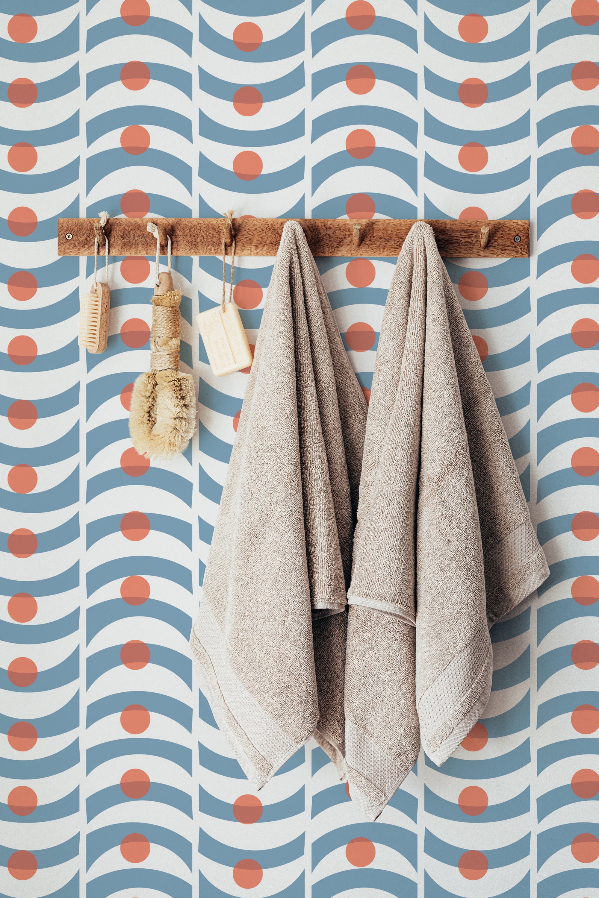 Self-adhesive vintage wallpaper with a geometric pattern of blue lines and orange circles, with a wooden towel rack and towels hung against it.