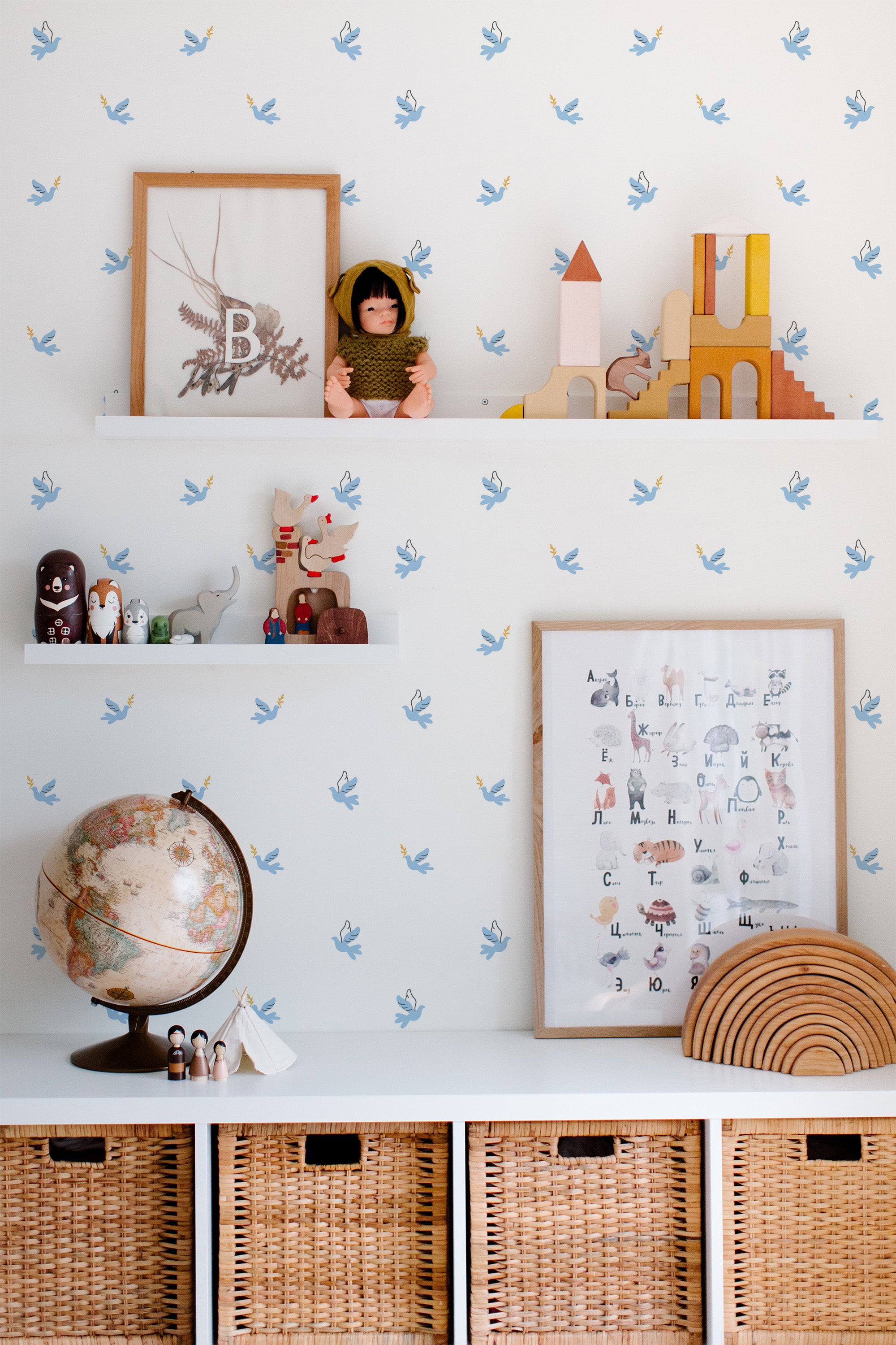 Self-adhesive wallpaper with a pattern of blue peace doves in flight on a light background, used in a children's room with decorative shelf and educational toys.