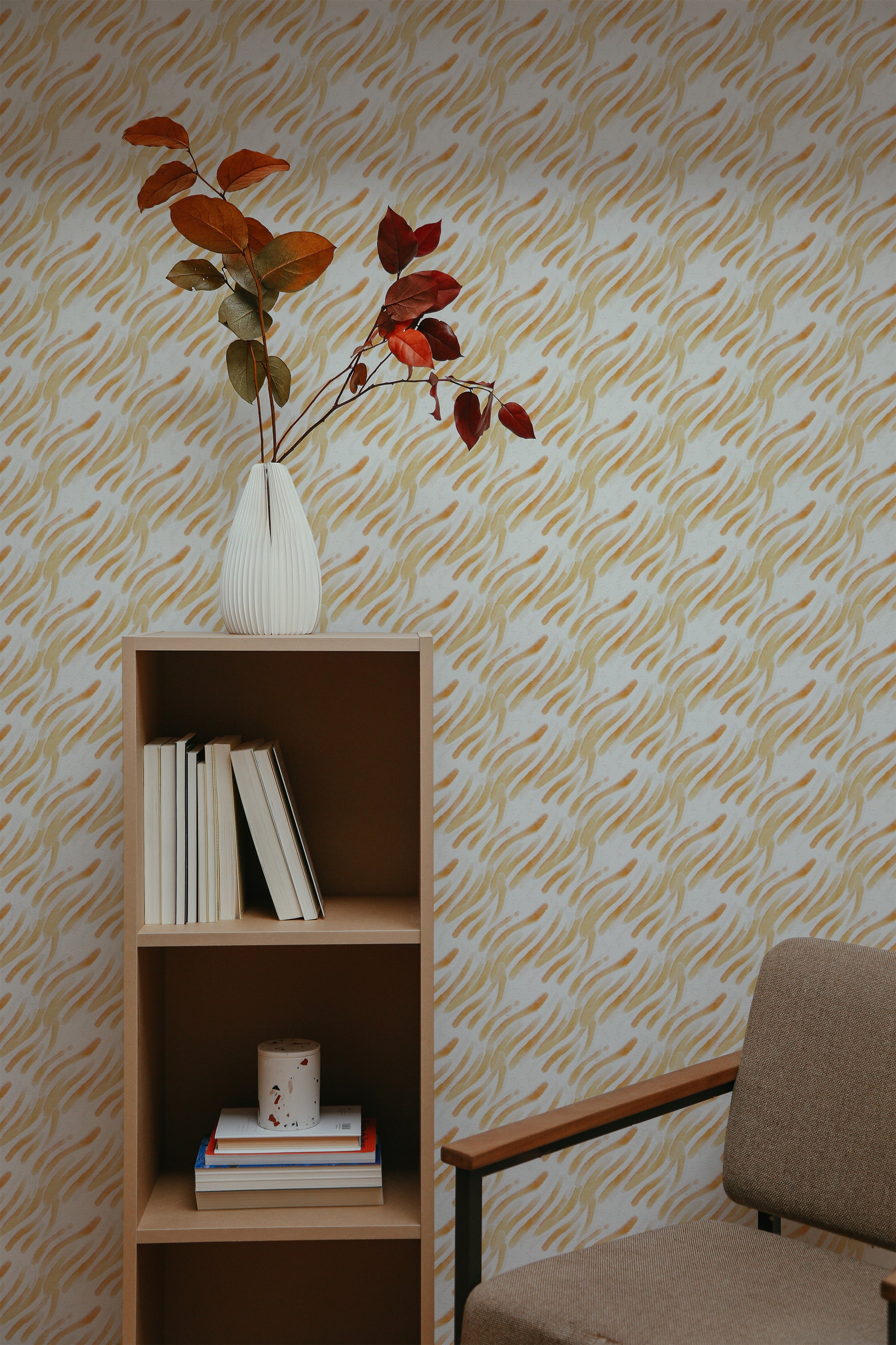 Self-adhesive wallpaper with yellow brush stroke pattern on a beige background, accenting a room with a wooden bookshelf and a chair.