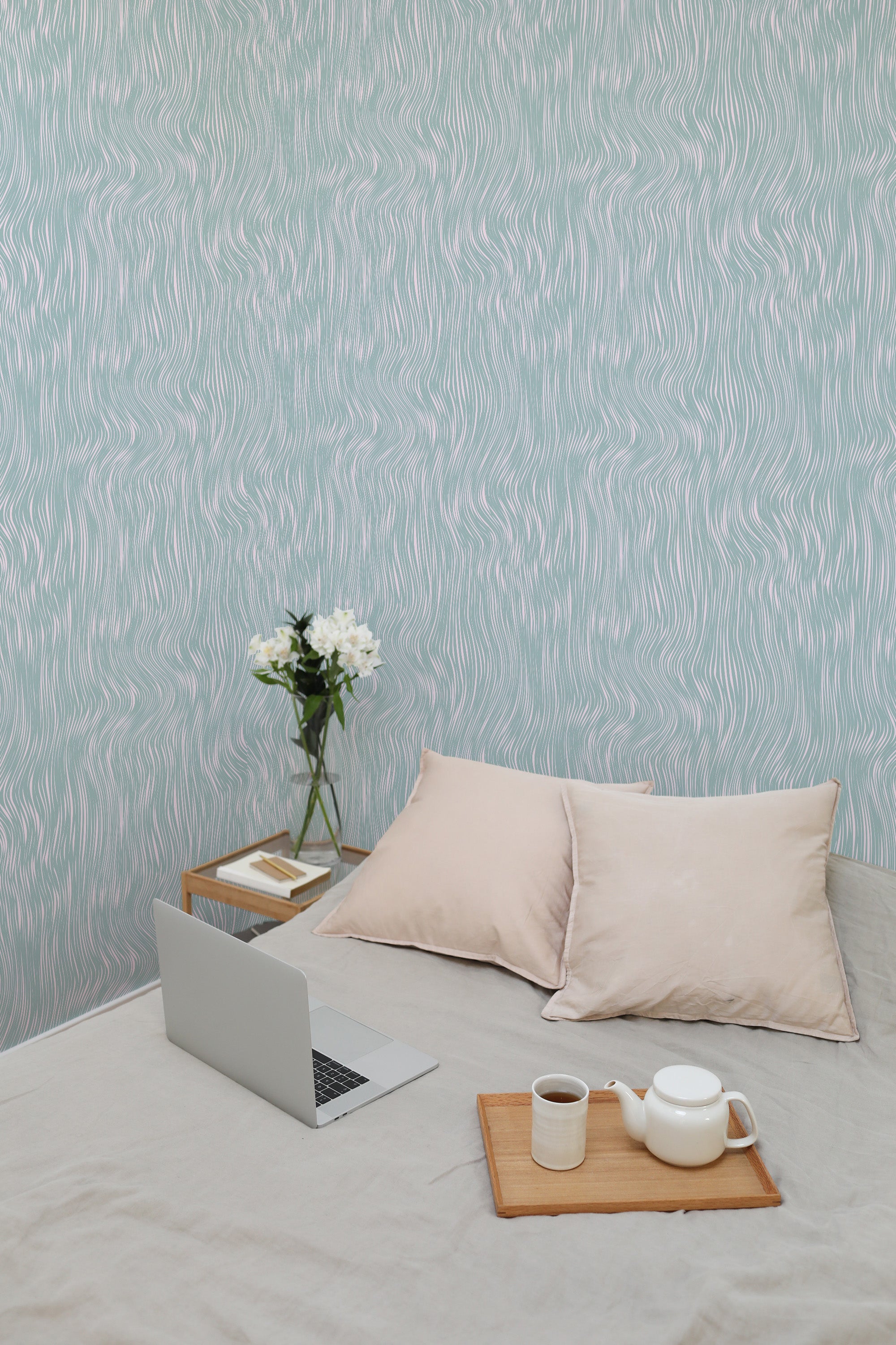 Self-adhesive wallpaper with a wavy neutral pattern on a room's wall, complementing the cozy interior with a laptop, pillows, and a tray with a teapot set.