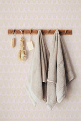 Self-adhesive Neutral Art Deco wallpaper with geometric pattern behind hanging towels and wooden rack with bath accessories.