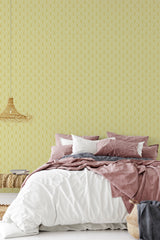 A bedroom with a wall covered in yellow Vintage Art Deco wallpaper with a geometric pattern, complementing the muted bedding and creating a classic ambiance with traditional wallpaper.