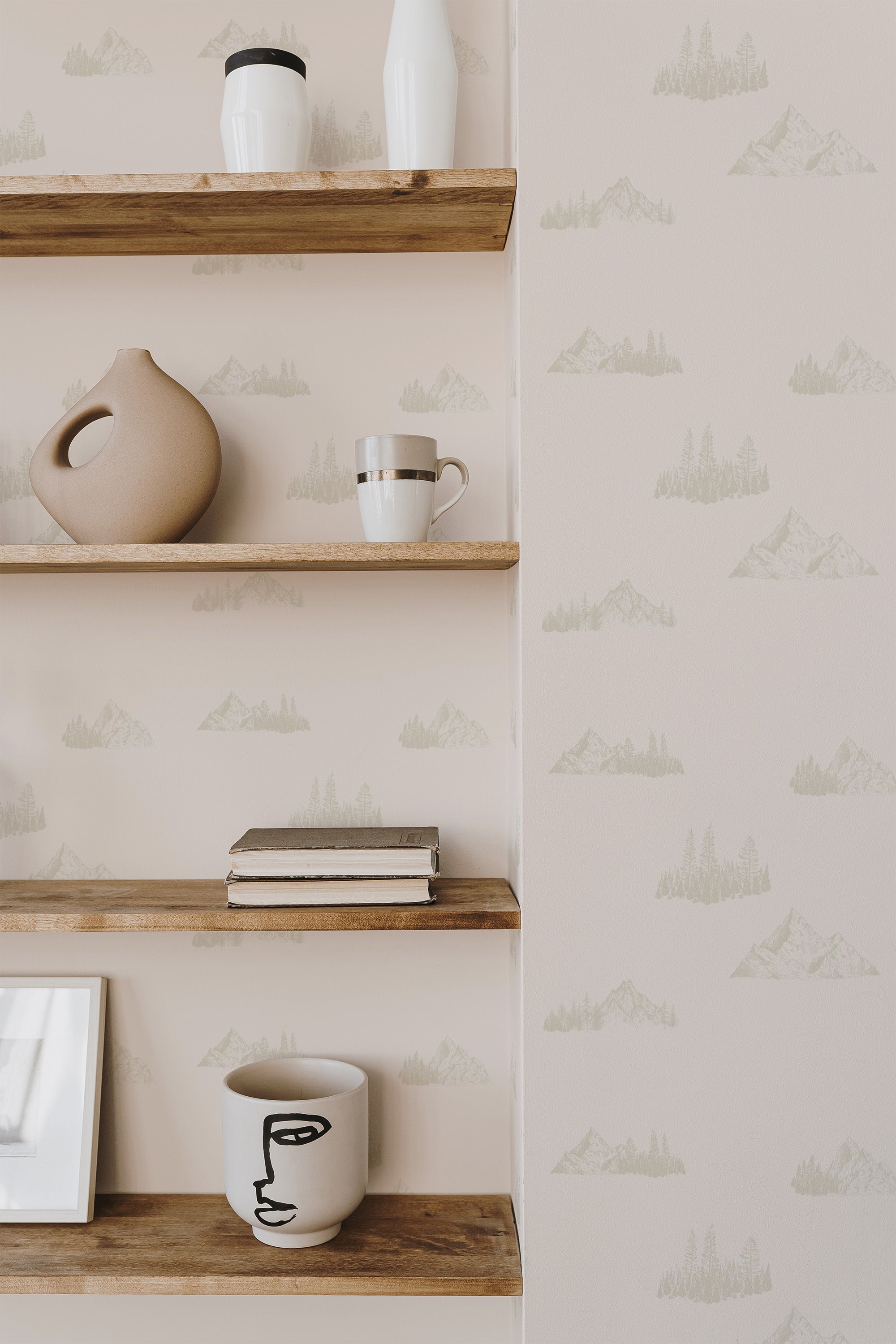 Self-adhesive wallpaper with a minimalist mountain pattern in light hues on a neutral background, accentuated by wooden shelves holding decorative items.