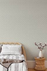 Self-adhesive wallpaper with a delicate berry pattern on a neutral background in a bedroom with a bed and a vase of cotton branches on a stool.