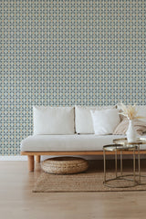 A room with one wall covered in Busy Tile wallpaper with a repetitive blue and beige geometric pattern, alongside a neutral-toned couch and a woven ottoman, embodying a traditional wallpaper.