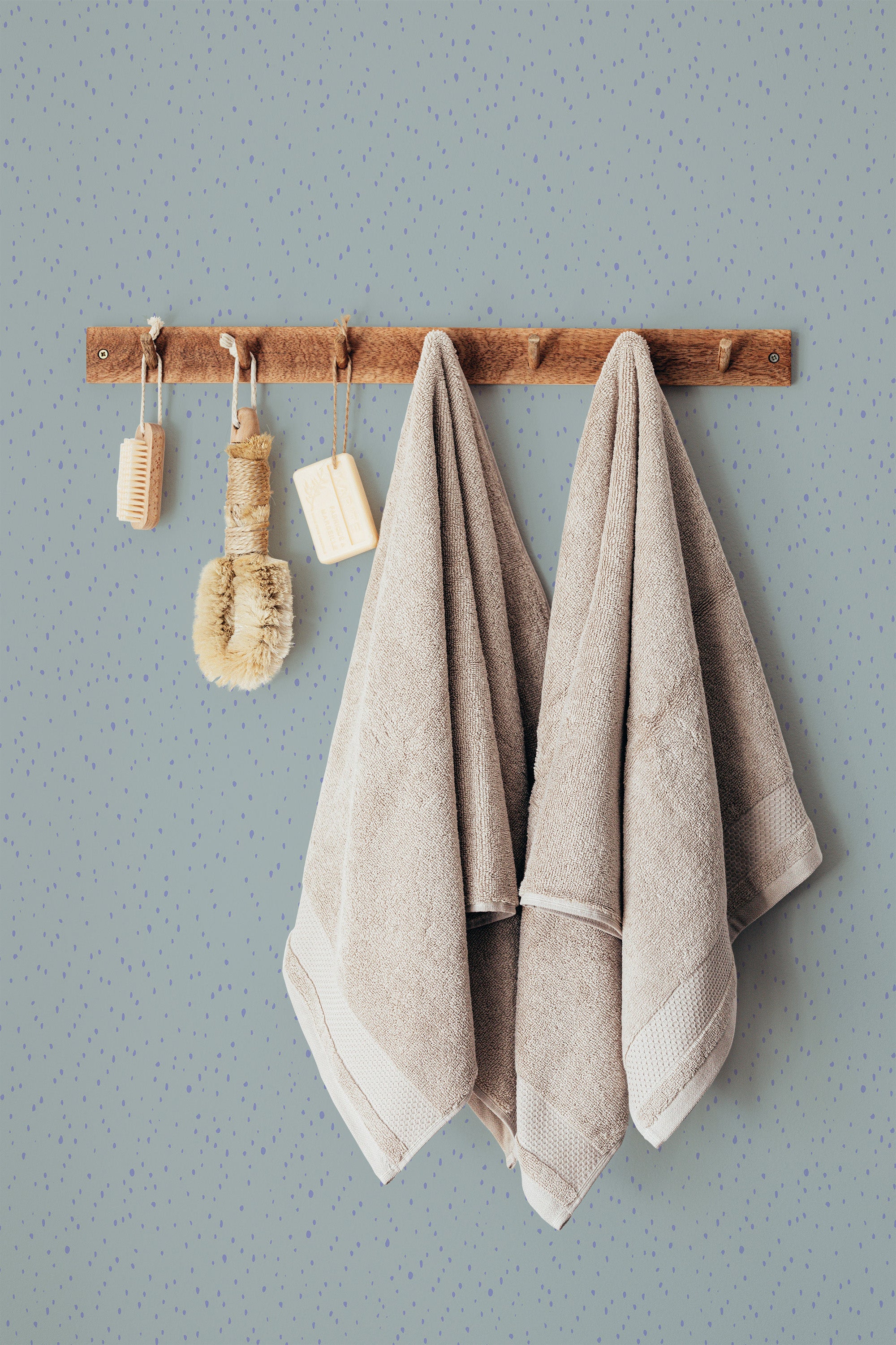 Self-adhesive wallpaper with a pattern of green and purple spots on a pastel background, behind a wooden rack holding towels and brushes.