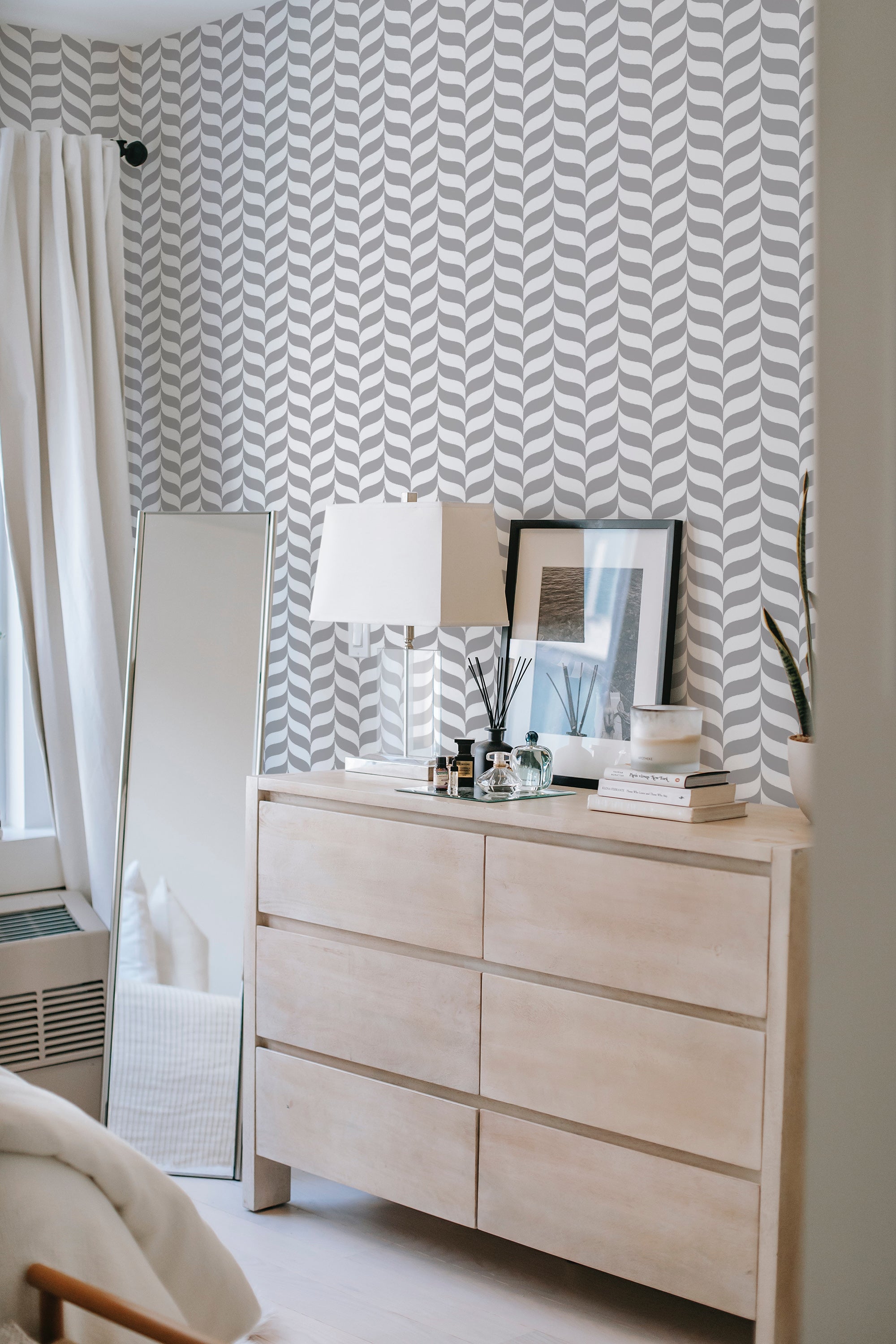 A room with a wall covered in elegant gray herringbone patterned wallpaper, complementing a light wood dresser and white decor, traditional wallpaper.