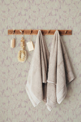 Self-adhesive pink tulip wallpaper with a subtle floral pattern behind a wooden rack holding two beige towels and bath brushes.