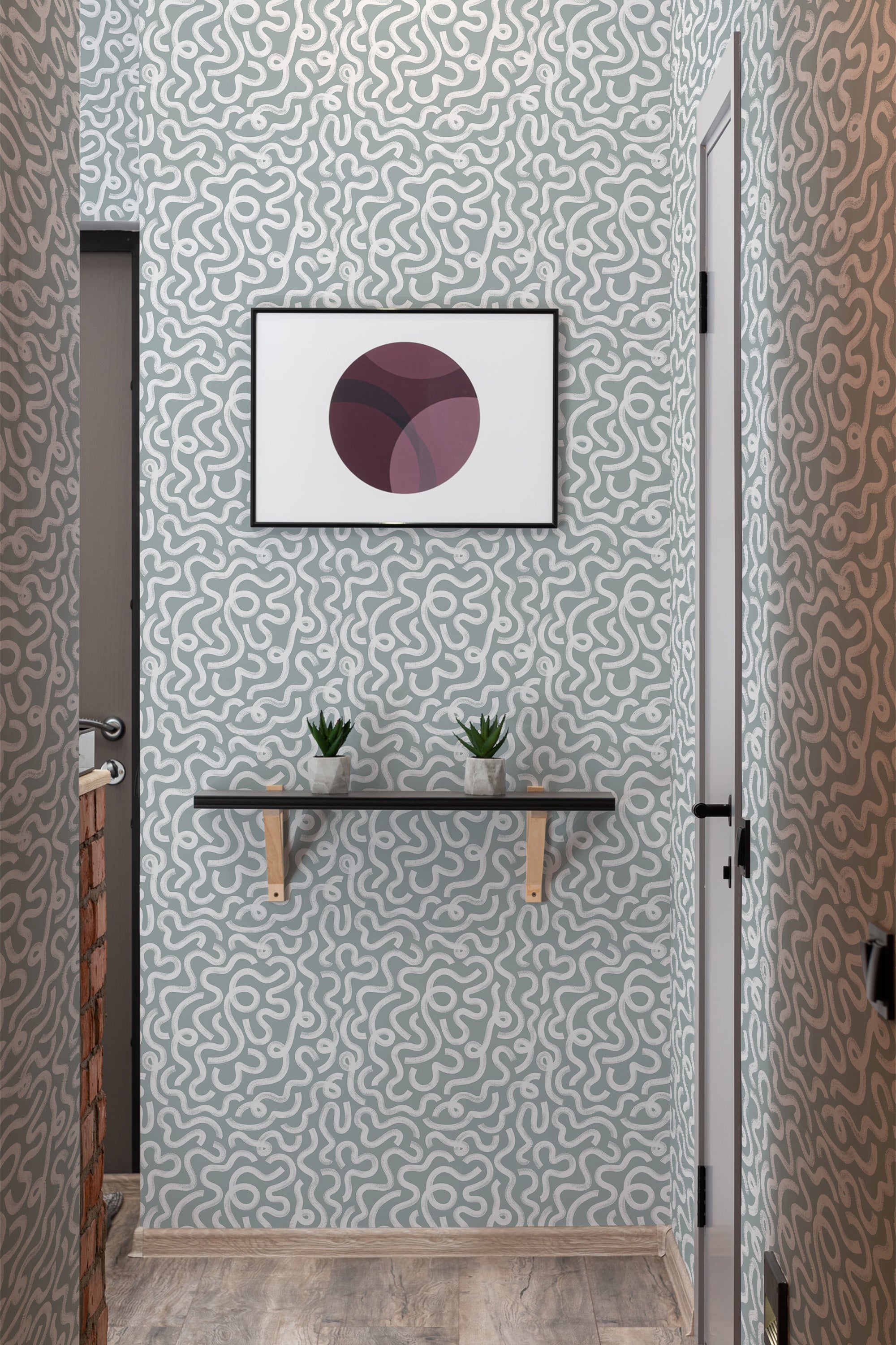 A room with Rainstorm brush lines design wallpaper with swirling gray patterns on a lighter background, complemented by a framed geometric artwork, a shelf with plants, and a traditional wallpaper finish.