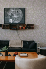 A cozy room with walls adorned with Abstract Neutral Flower wallpaper, combining soft hues and botanical patterns, above a dark sofa and wooden shelves, embodying a traditional wallpaper aesthetic.
