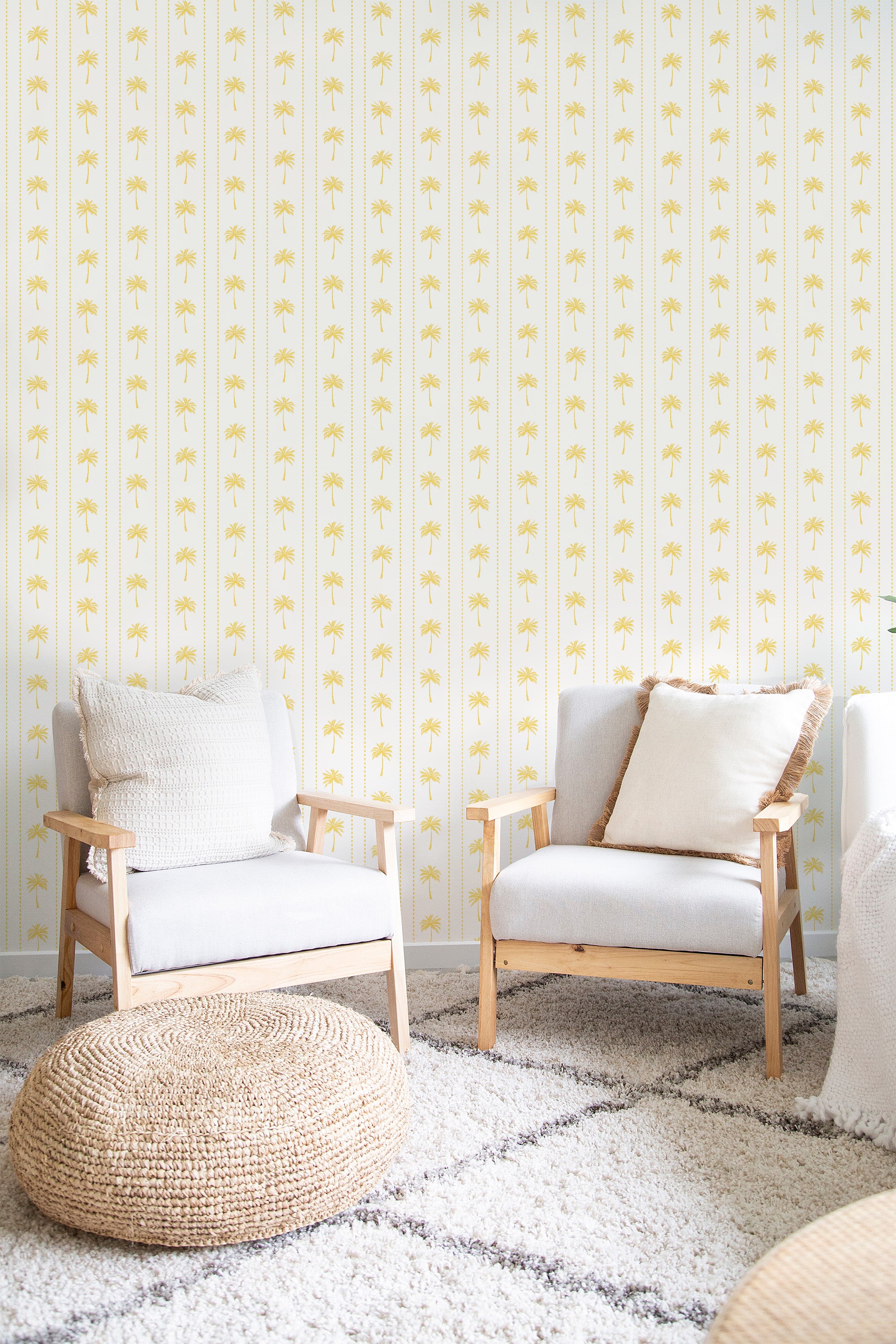 A room with white and yellow Vintage Sunny Palm wallpaper with repeated palm motifs, complemented by wooden armchairs and a woven ottoman, embodying a warm, tropical aesthetic in a traditional wallpaper.