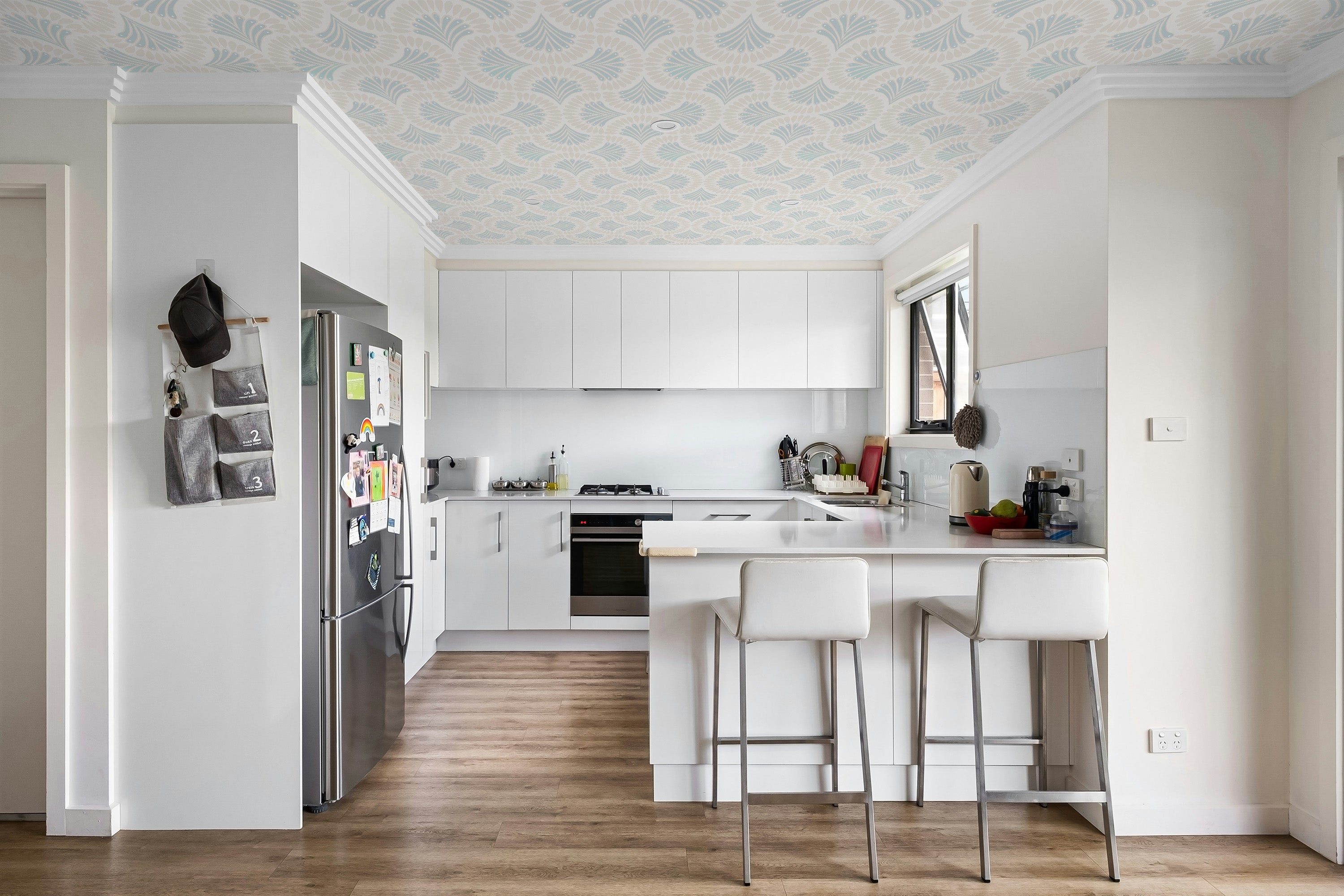 Modern kitchen with white cabinets, stainless steel appliances, and patterned ceiling wallpaper.