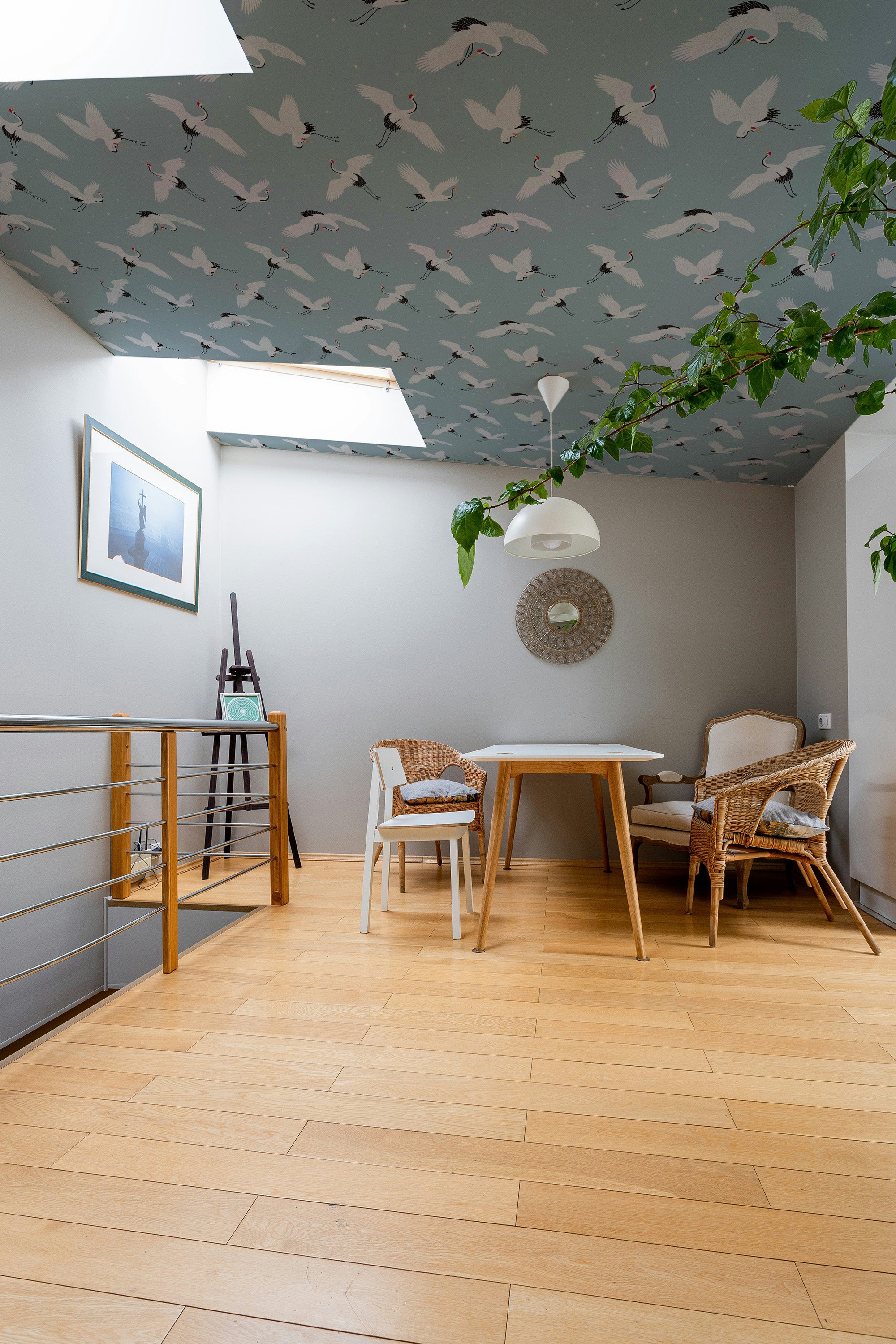 Modern dining area with wooden floor, table, and chairs against a light gray wall and blue ceiling wallpaper