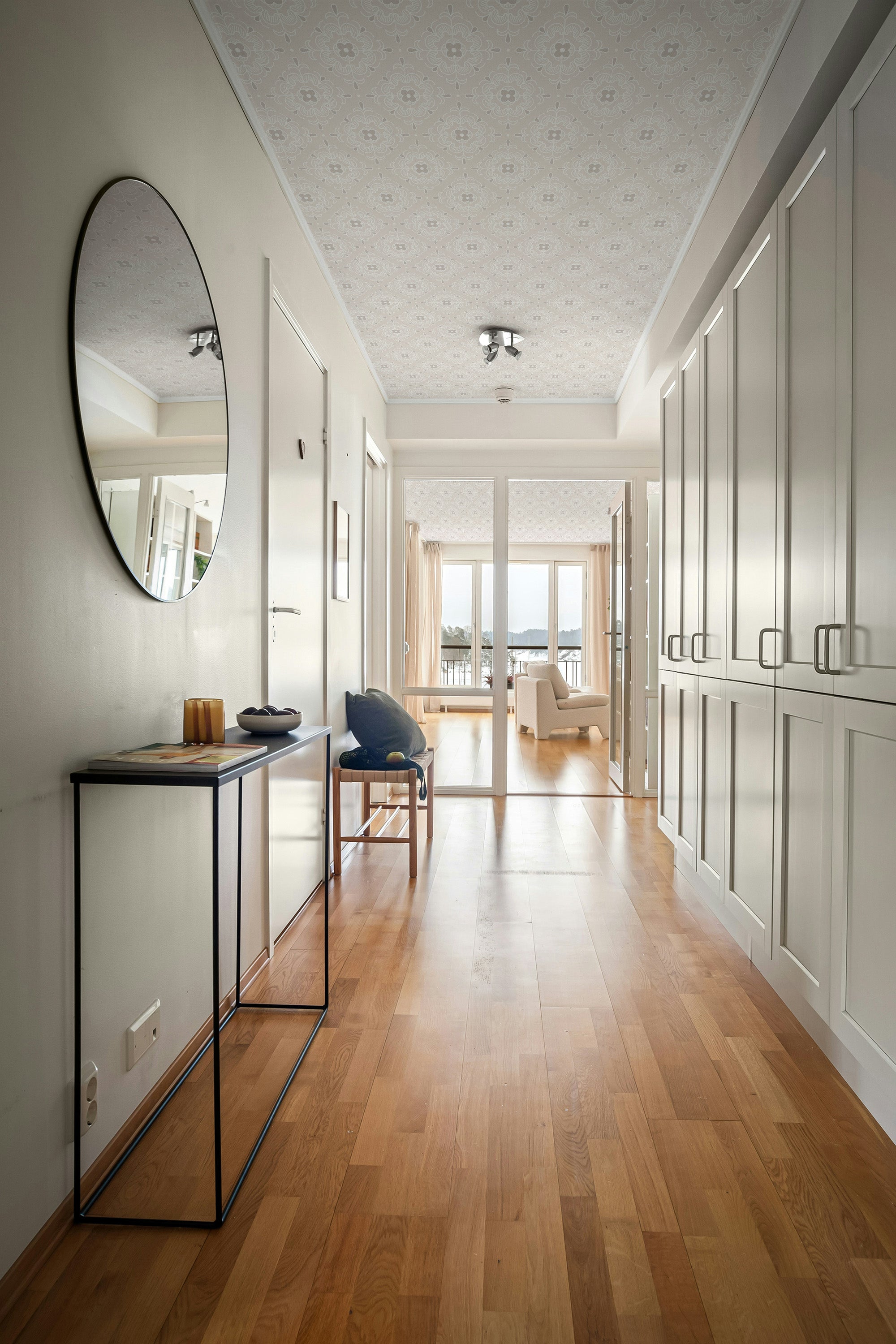 Modern interior hallway with ceiling wallpaper, wooden flooring, white walls, and a large mirror.