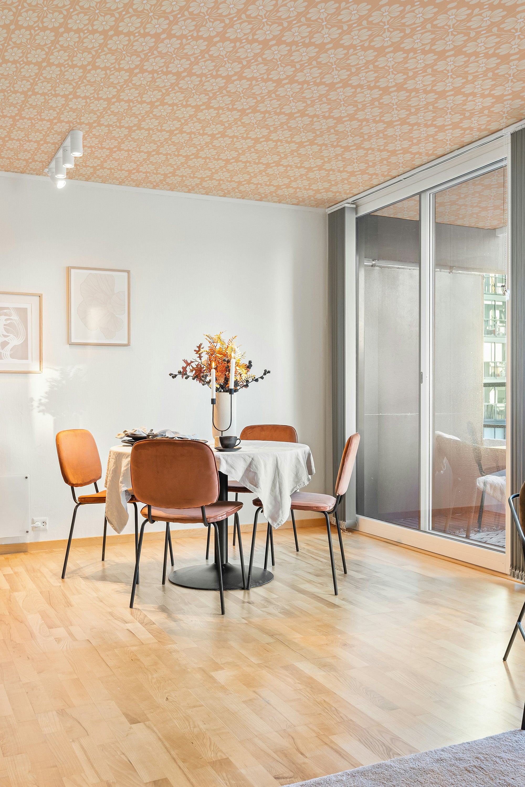 Modern dining room with wooden floor, round table, chairs and orange ceiling wallpaper.