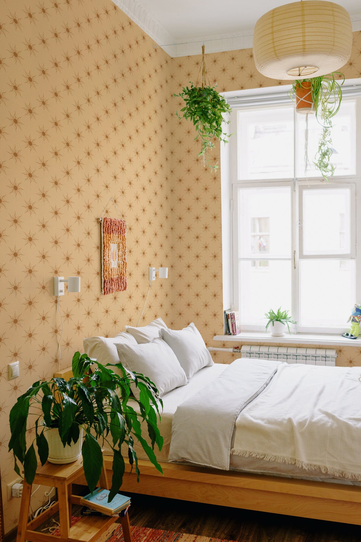 Radiant Sun Motifs grasscloth wallpaper on a bedroom wall, featuring small brown suns on a tan background.