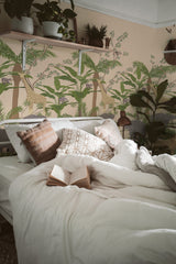 Tropical jungle animals and foliage design on bedroom wall, with a cozy bed and pillows in the foreground, peel and stick removable wallpaper.