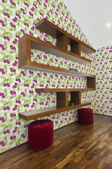 Cherry-themed wallpaper with clusters of bright red cherries hanging from green stems and leaves against a white background, complementing the warm wooden shelves and rich red stools in the room, evokes a traditional wallpaper.