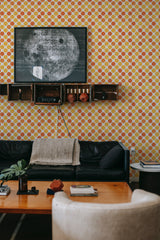 A wall covered in wallpaper with a pattern of evenly spaced yellow and orange dots set against a light background, creating a vibrant and lively atmosphere. The design appears in a geometric grid that gives the room a retro yet modern feel. Traditional wallpaper.