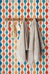 Self-adhesive wallpaper with a colorful retro design made up of wavy vertical stripes in shades of orange, blue, red, and cream.
