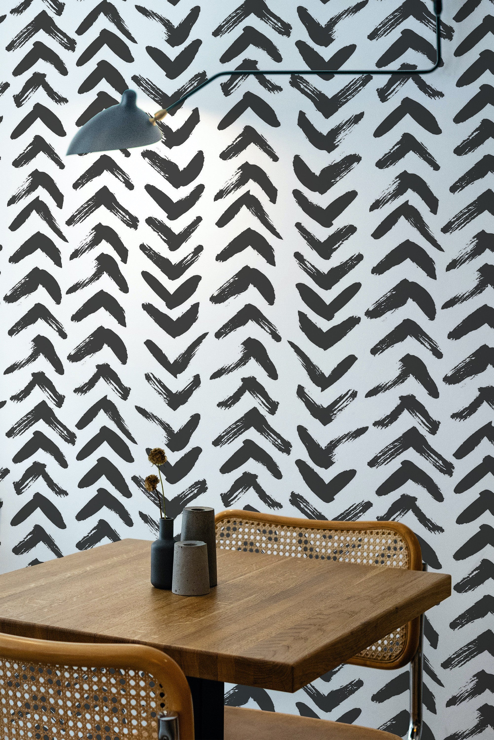 Self-adhesive wallpaper with a Brush Stroke Arrows design in black on a white background. The pattern features hand-drawn arrows pointing upwards, framing a warm, inviting dining area with wooden furniture.