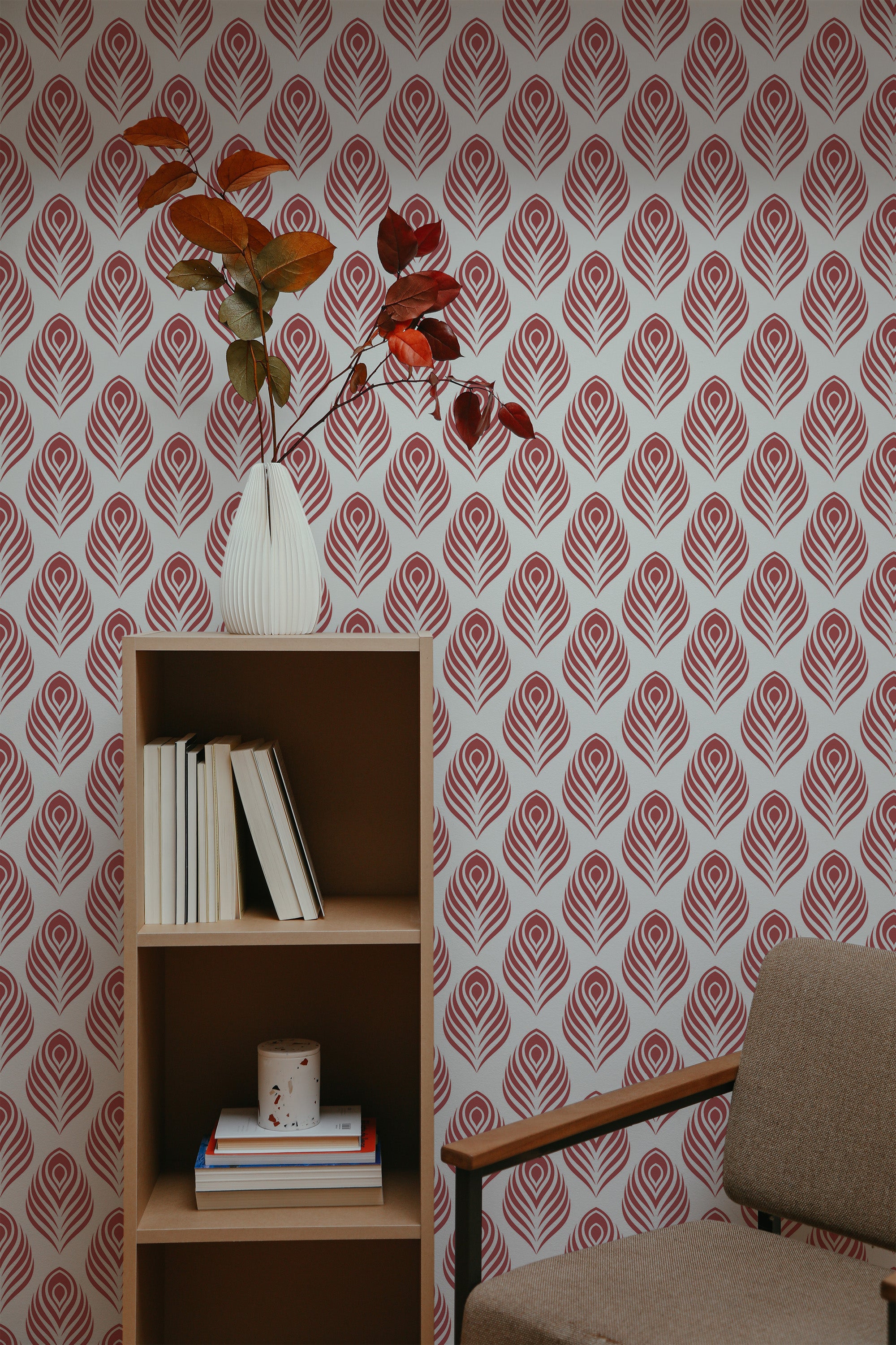 Self-adhesive wallpaper with a repeating red peacock feather pattern on a white background, complementing the room's decor with a brown shelving unit, books, vase, and a plant.