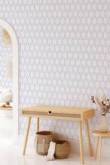 A room with a wall covered in a seamless botanical leaf pattern, intricately designed with repetitive, delicate leaf shapes in soft tones. The decor is complemented by neutral furnishings, including a light wood desk and woven baskets. Traditional wallpaper.