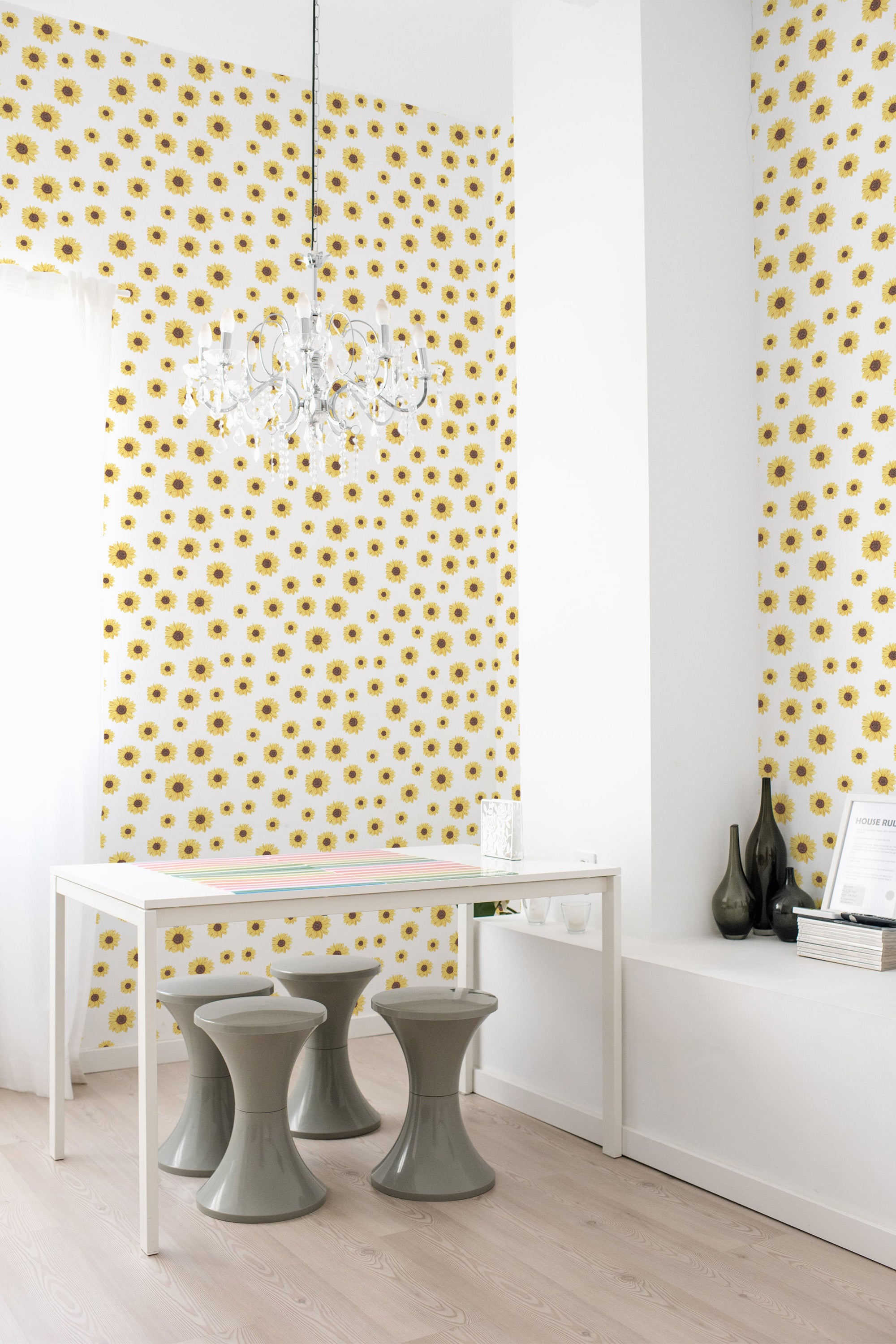 Wallpaper with a pattern of vibrant yellow sunflowers, each surrounded by green leaves, repeated across a white background, creating a bright and cheerful atmosphere in the room. Traditional wallpaper.