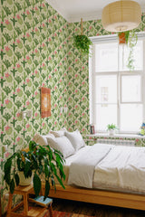 Wallpaper with a repeating cactus pattern in shades of green and pink accents, covering the entire wall around a bed with natural light coming from a large window. The design creates a lively, nature-inspired atmosphere in the room. Traditional wallpaper.