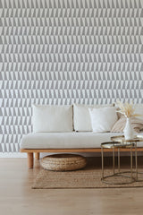 A room with wallpaper in a repeated geometric triangle pattern in various shades of gray, complementing a neutral-colored sofa and minimalist decor. Traditional wallpaper.