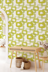 A room with 60s retro print wallpaper in shades of green and beige featuring an interlocking geometric pattern of rounded squares and ovals evoking a vintage aesthetic, traditional wallpaper.