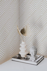 Self-adhesive geometric wallpaper with gold lines forming a zigzag and maze-like pattern on a light beige or off-white background, enhancing a modern and elegant aesthetic in the room.
