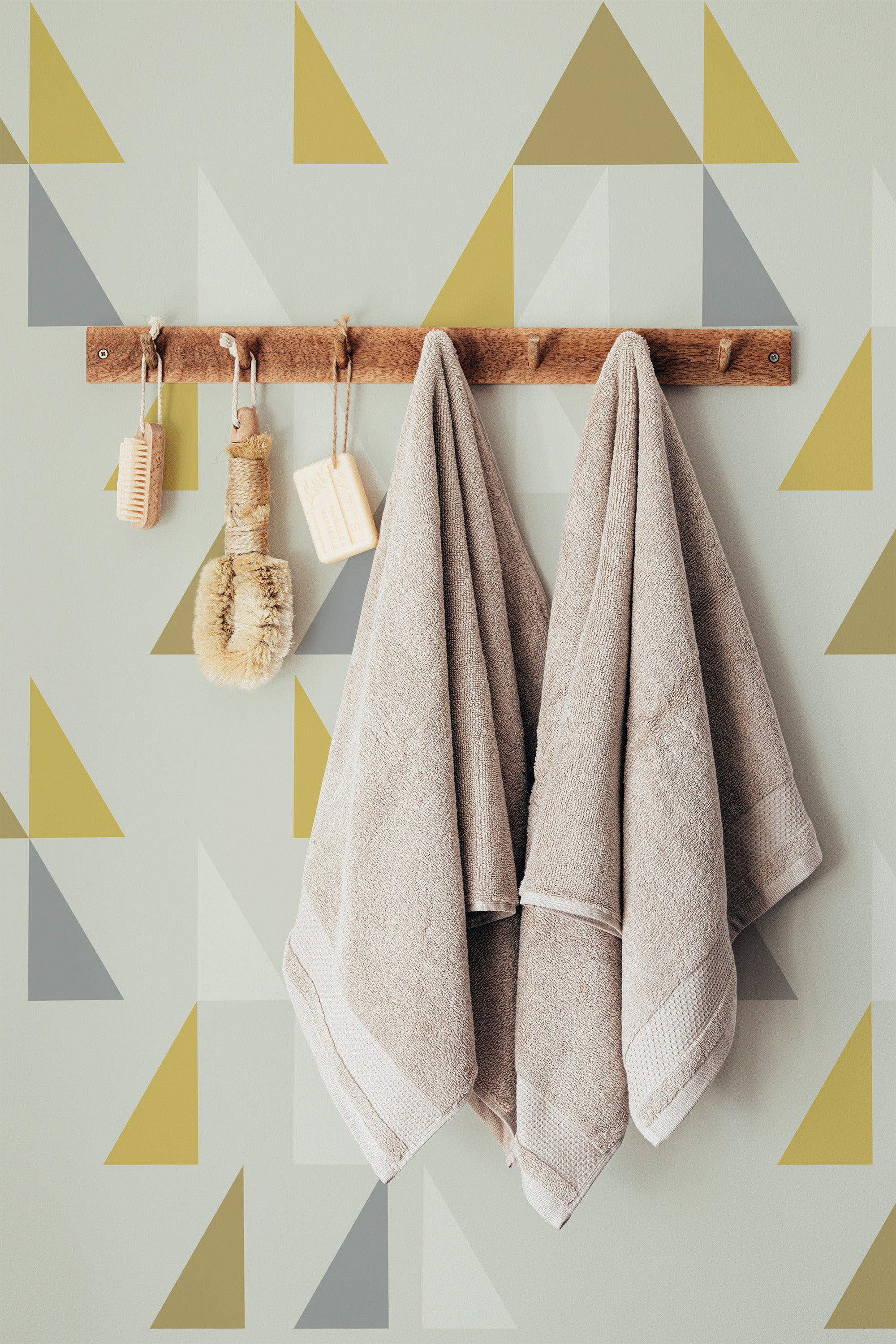 Self-adhesive wallpaper with a design of overlapping triangles in muted shades of yellow, gray, and beige on a light background.