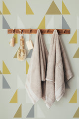 Self-adhesive wallpaper with a design of overlapping triangles in muted shades of yellow, gray, and beige on a light background.