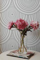 Self-adhesive wallpaper with an Optic Circle design in gray patterns, creating a geometric, hypnotic effect on the wall, behind a clear glass vase holding pink peonies.