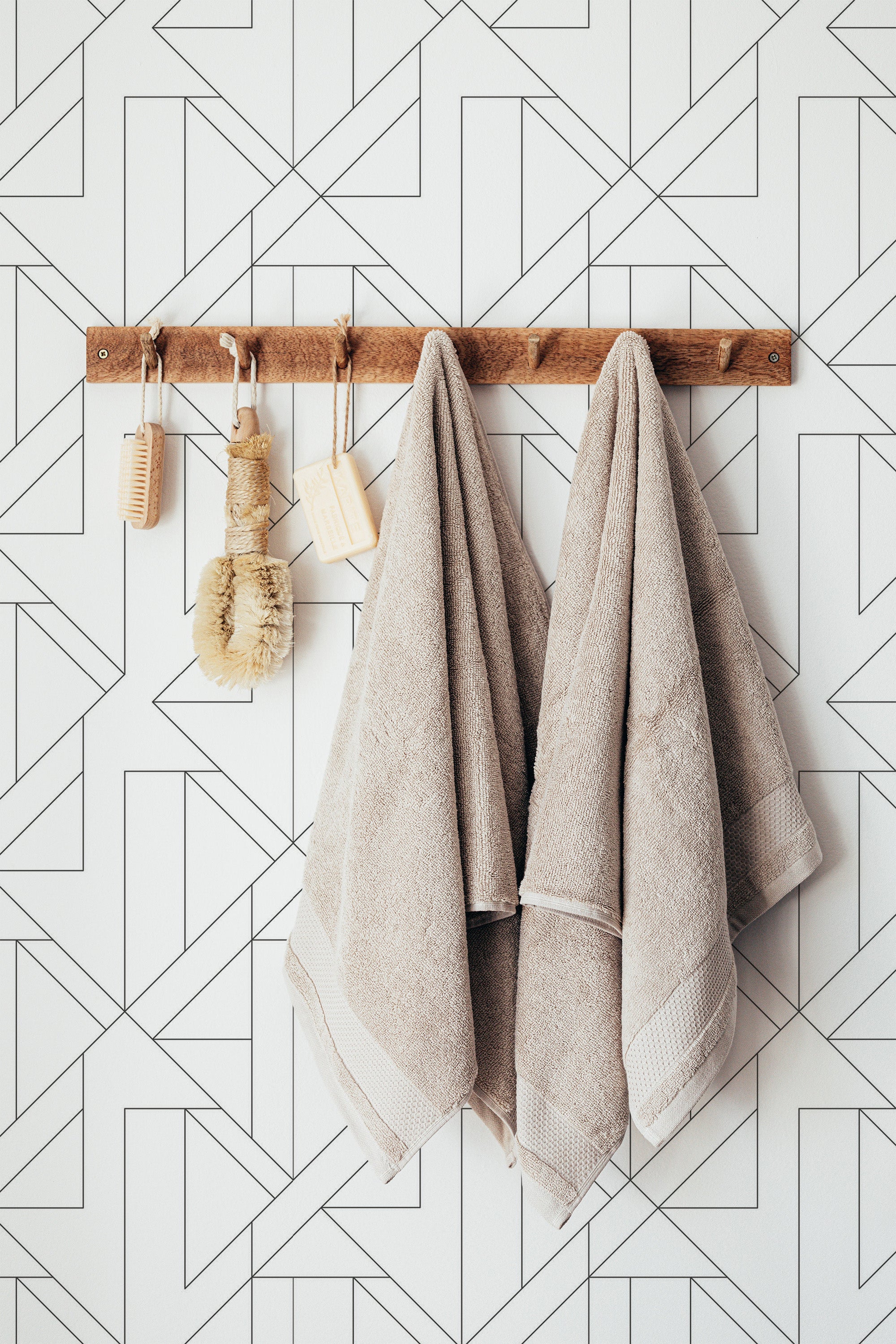 Self-adhesive geometric art deco wallpaper with sharp lines and angles in a black and white color scheme, towels hanging on a wooden rack.