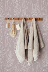 Self-adhesive wallpaper with a white gladiolus pattern on a muted purple background, with towels hanging on a wooden rack in front.