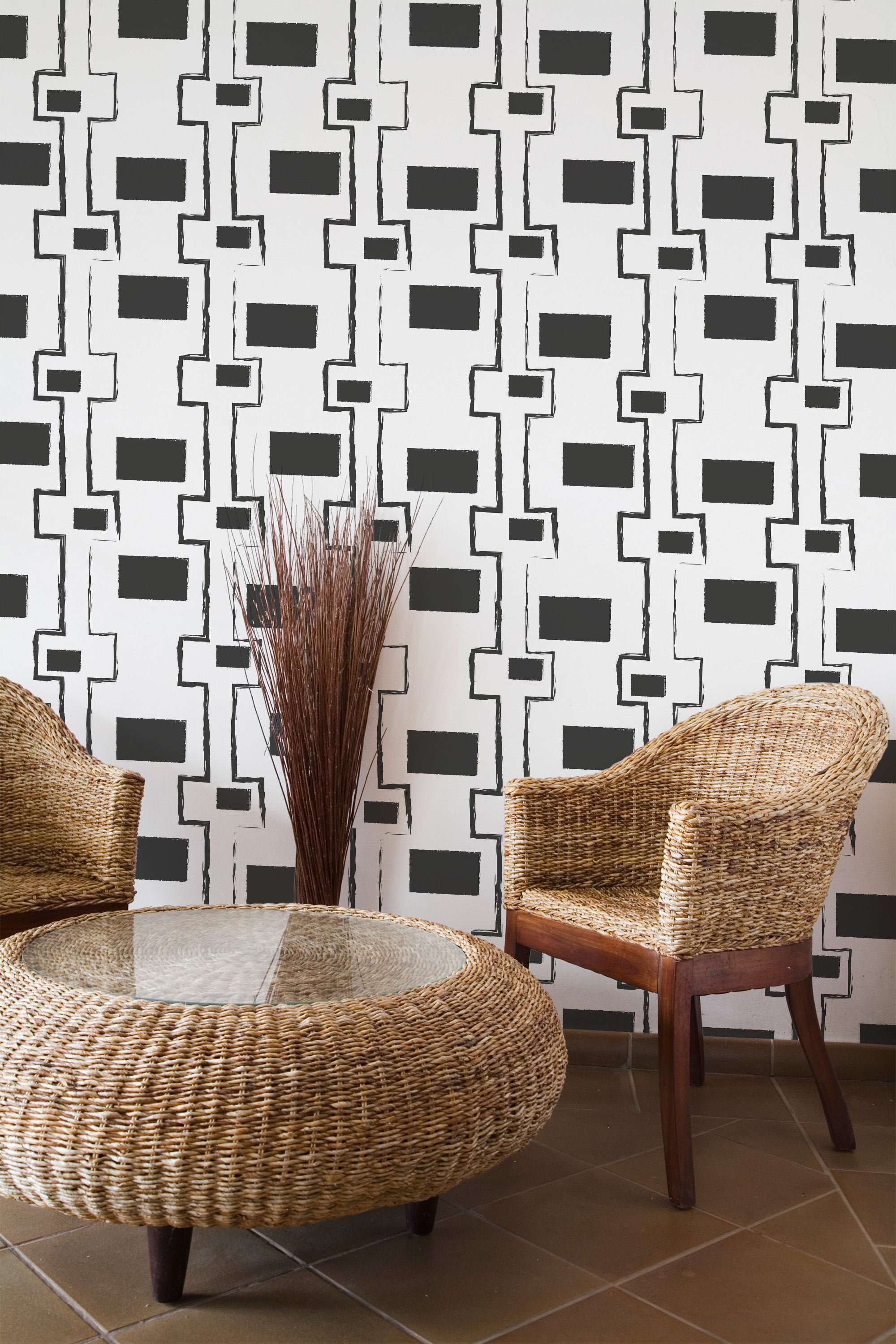 Self-adhesive wallpaper with a bold geometric pattern of black and white angular shapes on a room wall, complemented by wicker chairs and a vase with twigs.