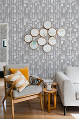 A cozy room with a wall covered in a leaf arrow patterned wallpaper, complemented by a modern chair with yellow accent cushions, a side table, and a sofa set against a traditional wallpaper.