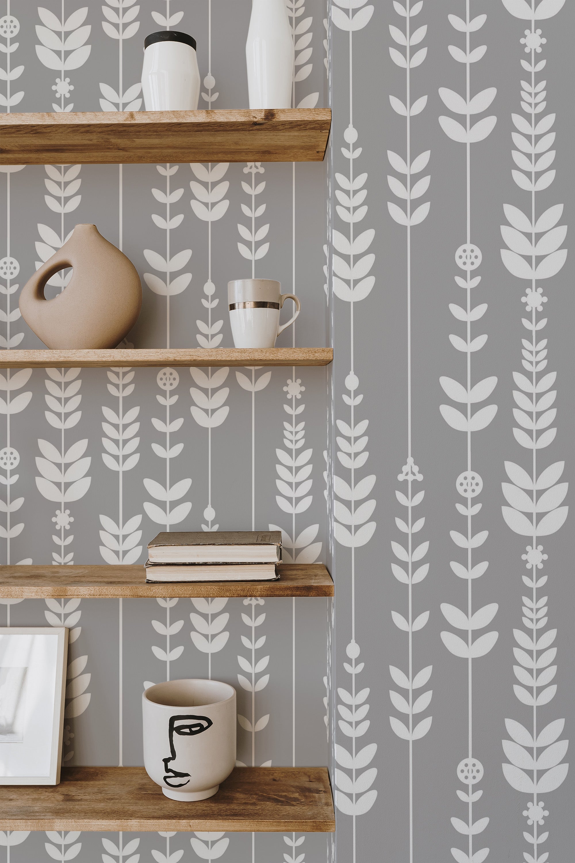 Self-adhesive wallpaper with a leaf arrow pattern in shades of grey, affixed behind wooden shelves adorned with decorative items.