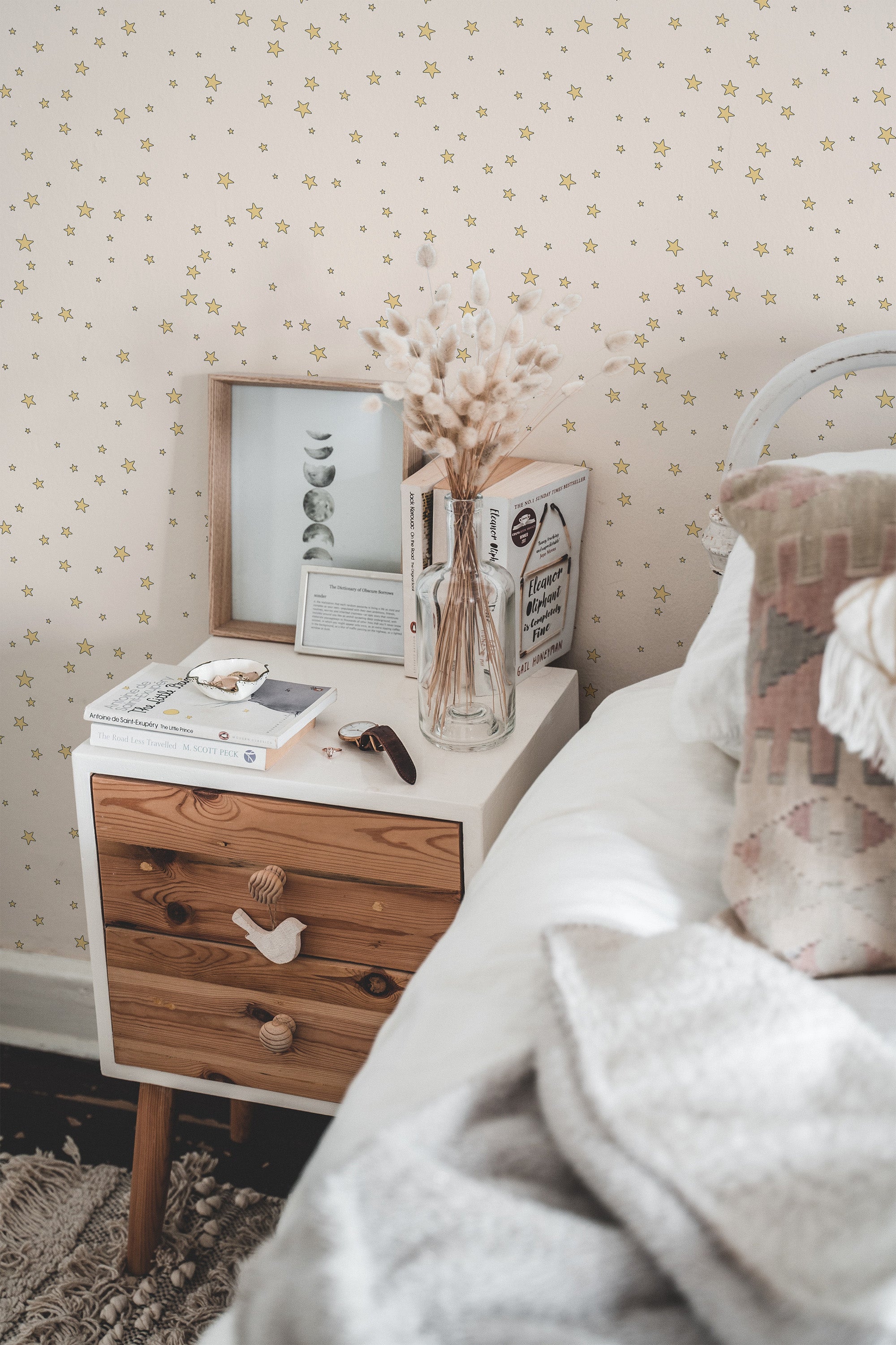 Self-adhesive nursery stars wallpaper with a pattern of small, gold stars scattered on a light background, covering a wall beside a bed and nightstand.