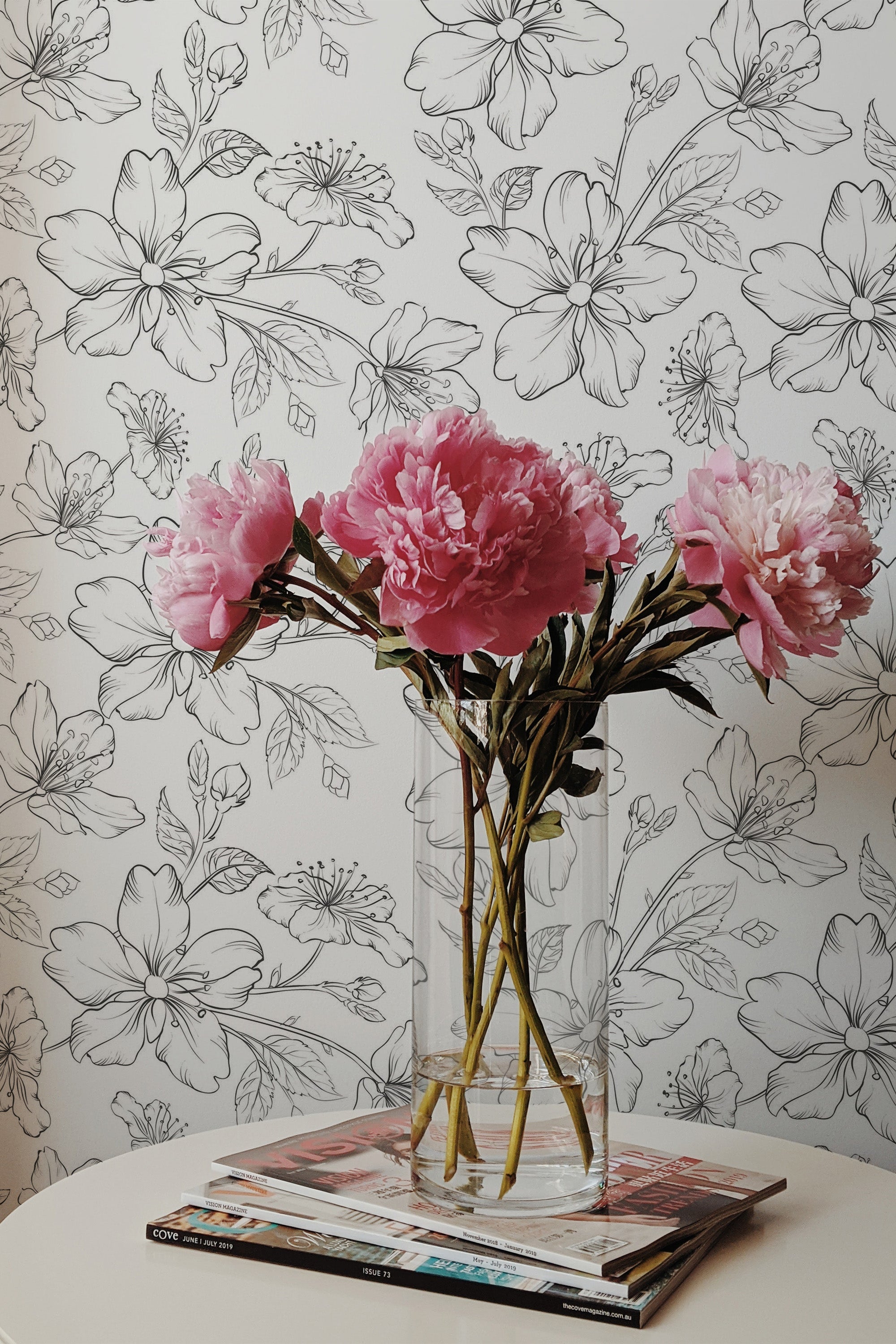 Self-adhesive floral nursery wallpaper with hand-drawn style monochrome flowers, complemented by a bouquet of pink peonies in a clear vase.